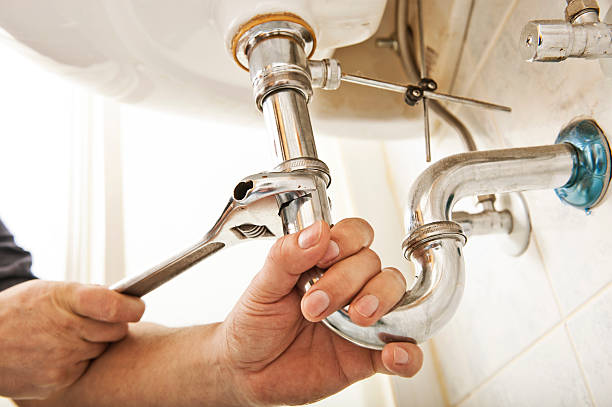 plumber using a wrench to tighten a siphon under a sink
